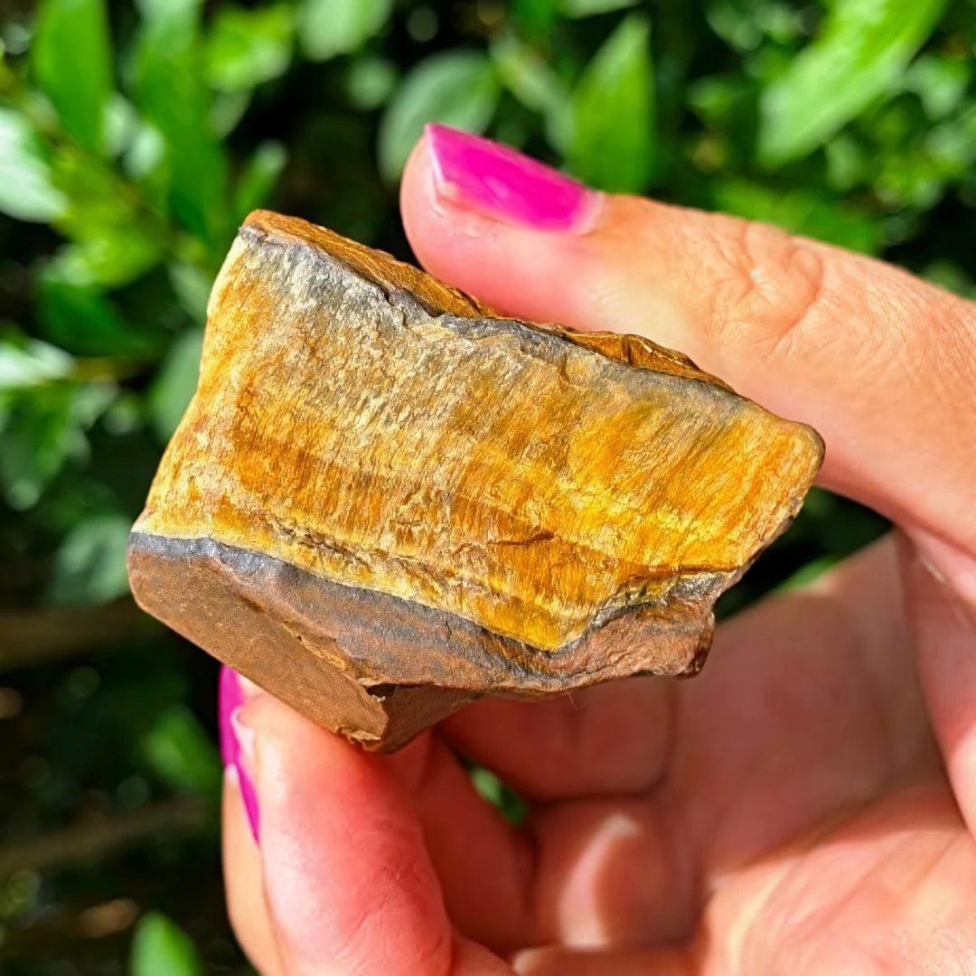 Hand holding a raw Tiger Eye crystal, showcasing its silky golden-brown bands for grounding and courage.