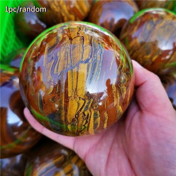 Polished Tiger Iron crystal sphere with golden shimmer, deep red, and metallic silver bands, held in a hand.