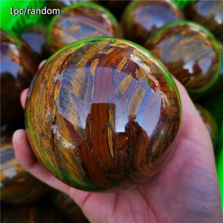 Polished Tiger Iron crystal sphere with golden shimmer, deep red, and metallic silver bands, held in a hand.