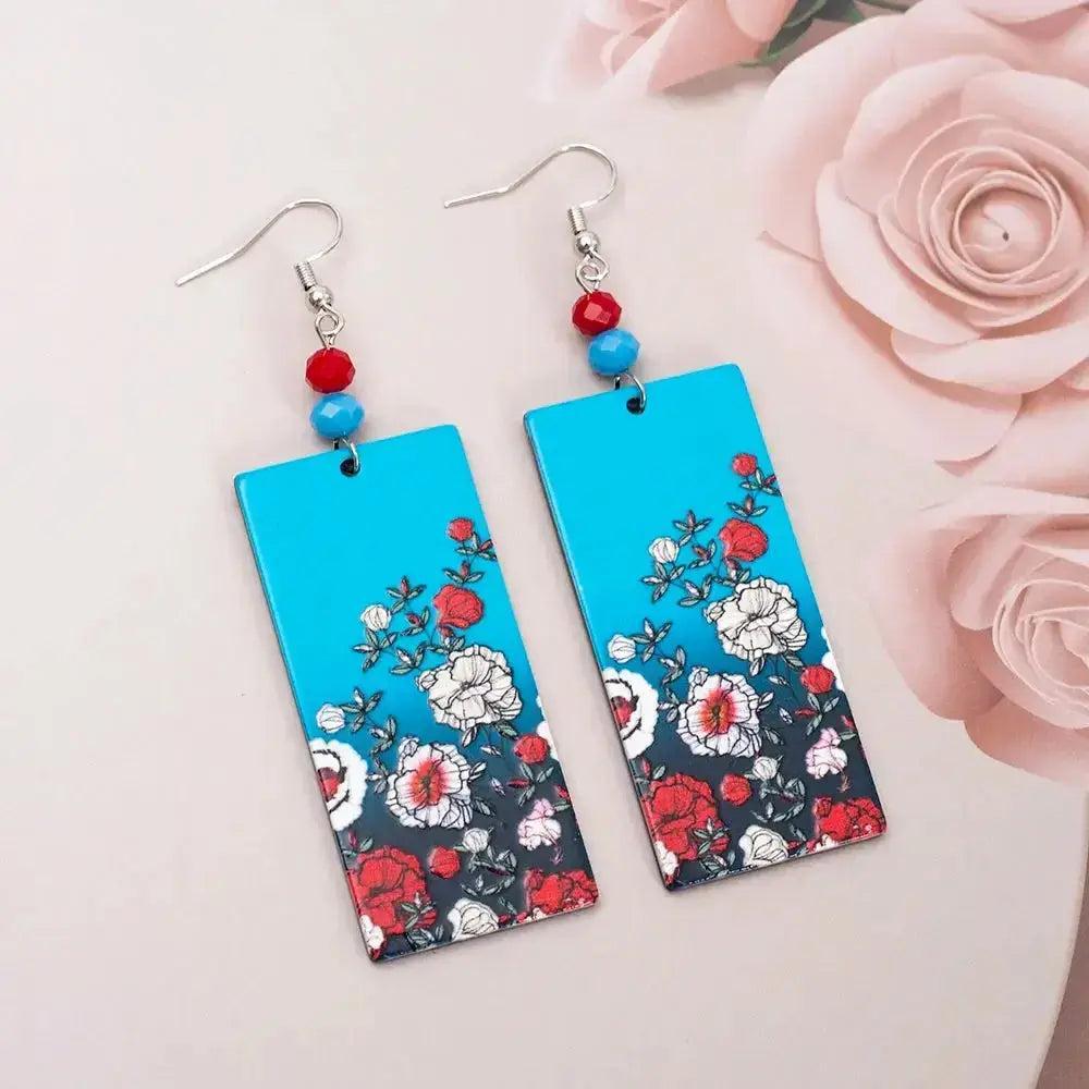 Vibrant rectangular acrylic earrings with red and white floral designs on a blue background, accented with red and blue beads.