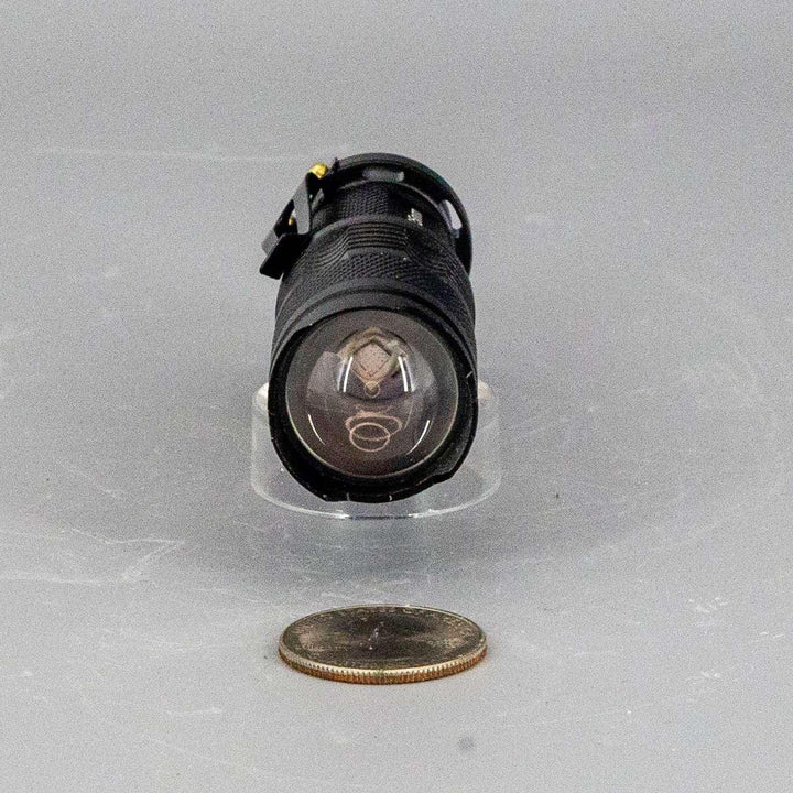 Compact black UV-365nm AA battery flashlight with clear lens, shown next to a quarter for scale.