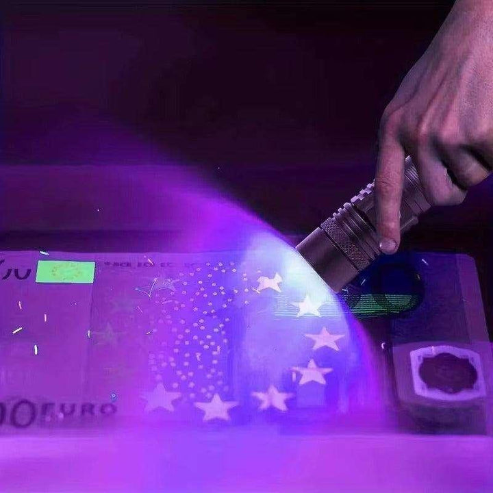 Hand holding a silver UV-365nm AA flashlight illuminating a euro banknote, revealing fluorescent security features.