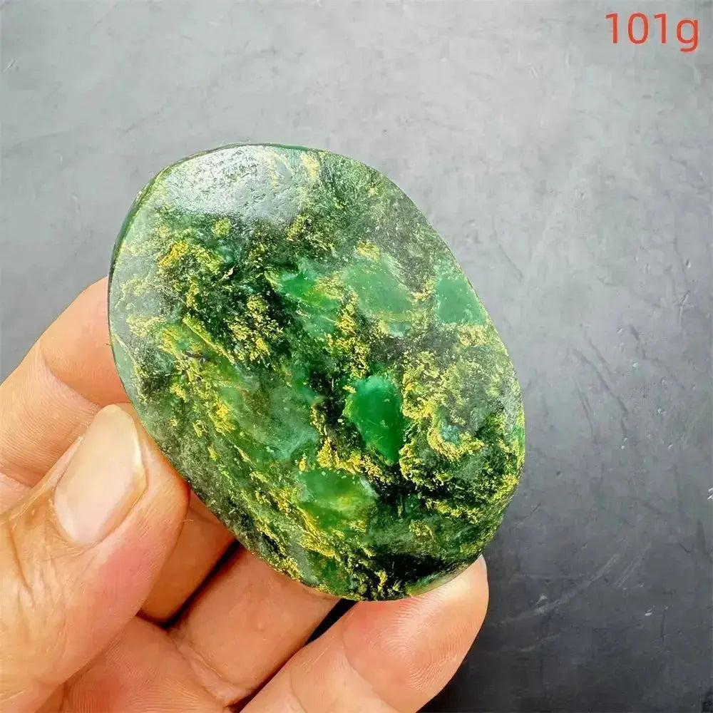 Polished Verdite crystal palm stone, deep mottled green with gold and rust flashes, held in a hand.