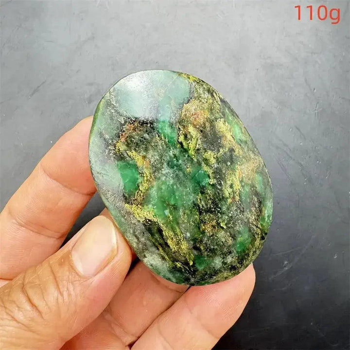 Polished Verdite crystal palm stone, deep mottled green with gold and rust flashes, held in a hand.
