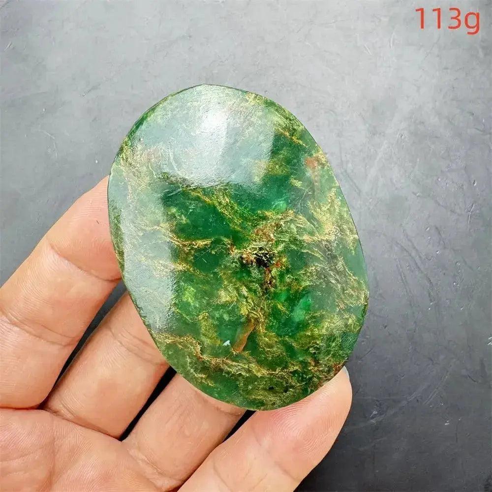 Polished Verdite palm stone, deep mottled green with gold and rust flashes, held in a hand.