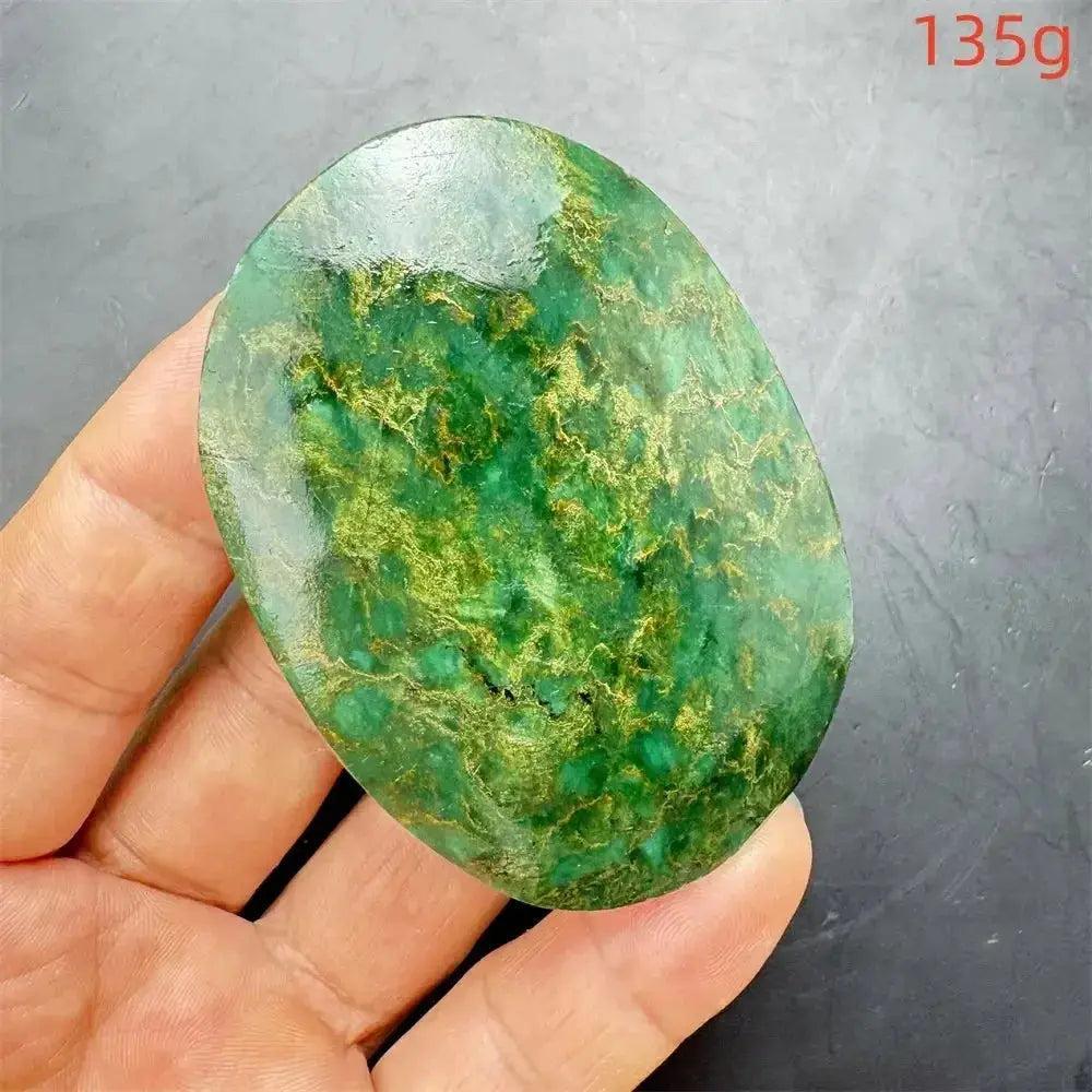 Polished Verdite crystal palm stone, deep mottled green with gold and rust flashes, held in a hand. 135g.