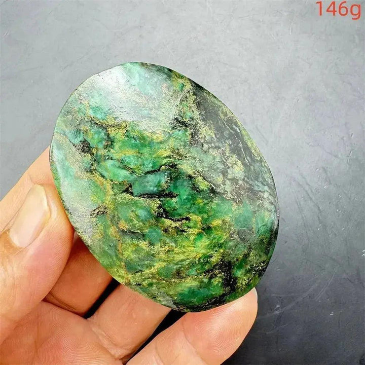 Polished Verdite palm stone, deep mottled green with gold and black veins, held in a hand.