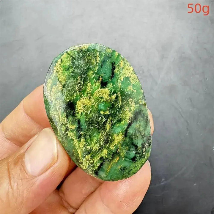 Polished Verdite palm stone, deep mottled green with golden-yellow and black accents, held in a hand.