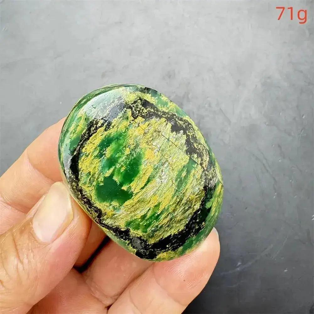 Polished Verdite palm stone, deep mottled green with yellow and black patterns, held in a hand.