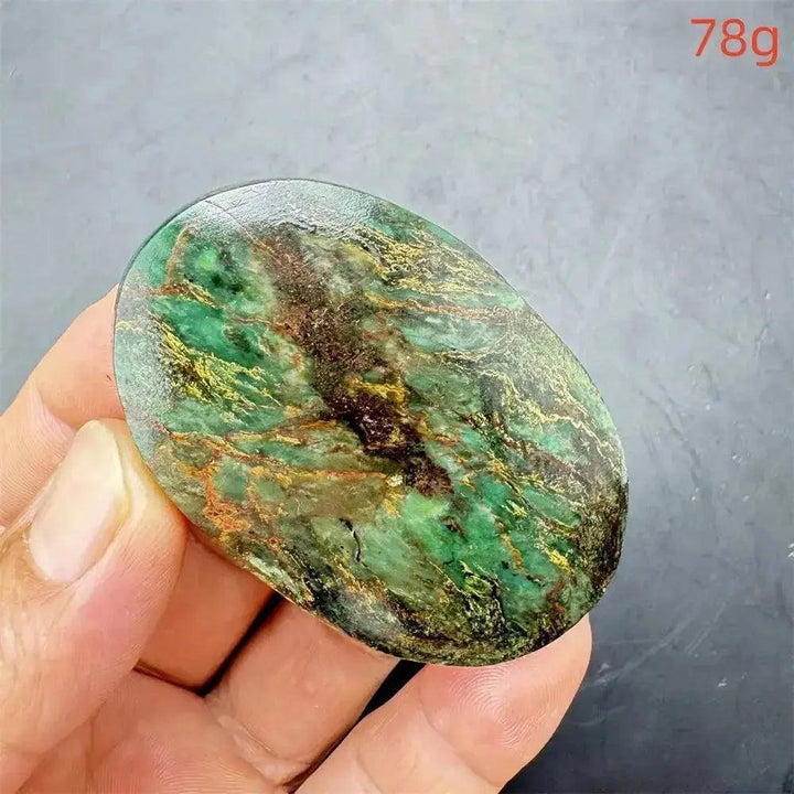 Polished Verdite palm stone, deep mottled green with gold and rust flashes, held in a hand.
