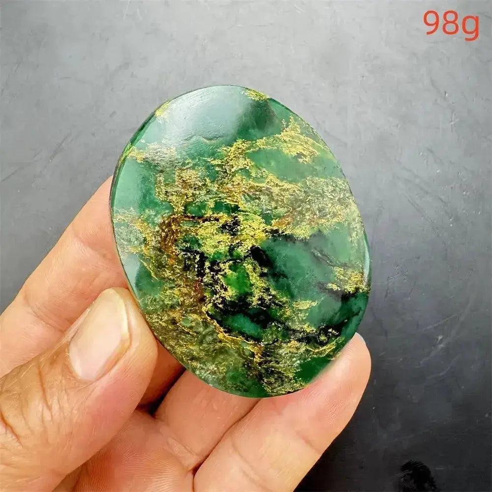 Polished Verdite crystal palm stone, deep mottled green with golden and rust flashes, held in a hand.
