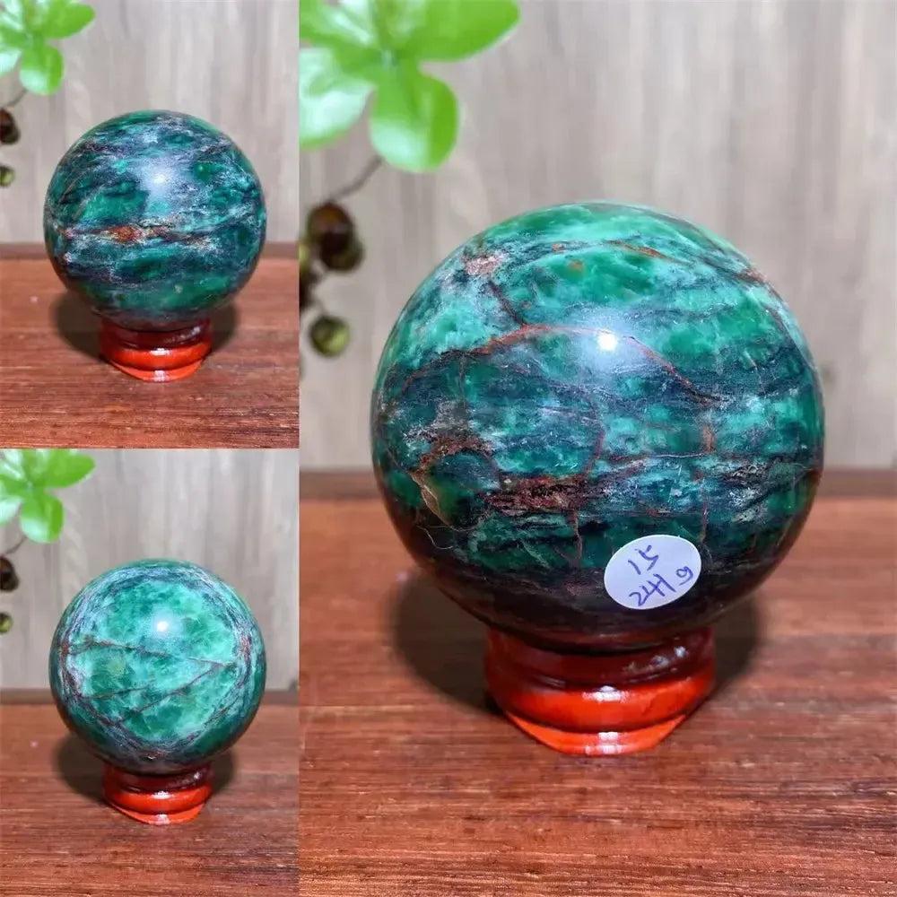 Verdite sphere with deep forest green and shimmering gold veins on a reddish-brown wooden stand.