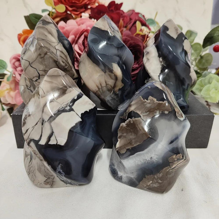 Five polished volcanic agate flame crystals in charcoal, cream, and brown, with floral background.