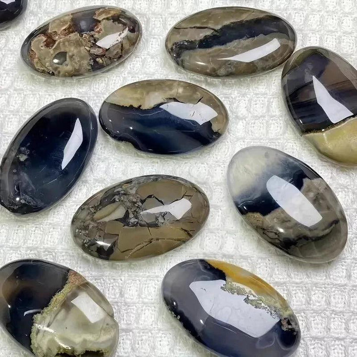 Polished natural volcanic agate palm stones in various earthy tones, some with fluorescent UV reactive properties.