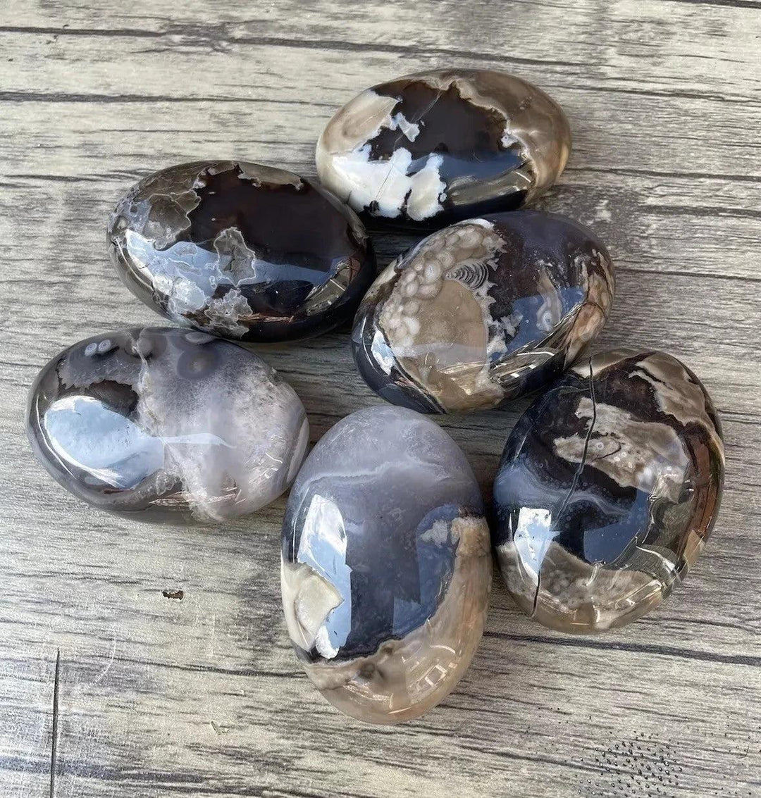 Polished natural volcanic agate palm stones in various black, white, and gray patterns, ideal for home decor.