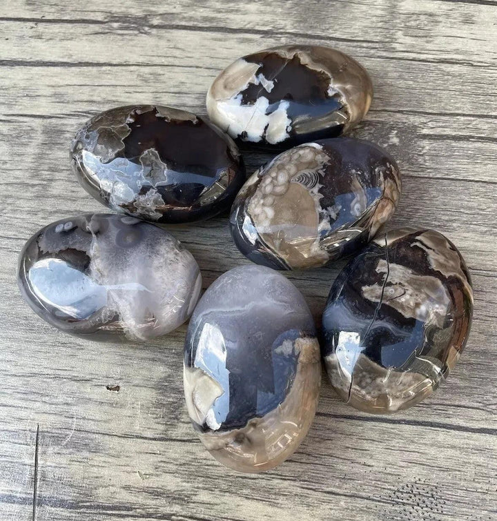 Polished natural volcanic agate palm stones in various black, white, and gray patterns, ideal for home decor.