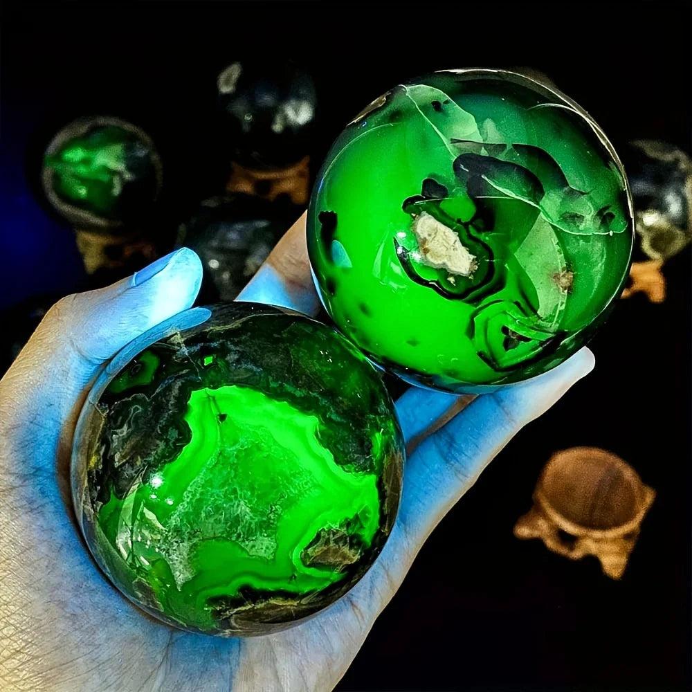 Hand holding two glowing green UV reactive volcanic agate spheres, 50-80mm, for grounding and stability.
