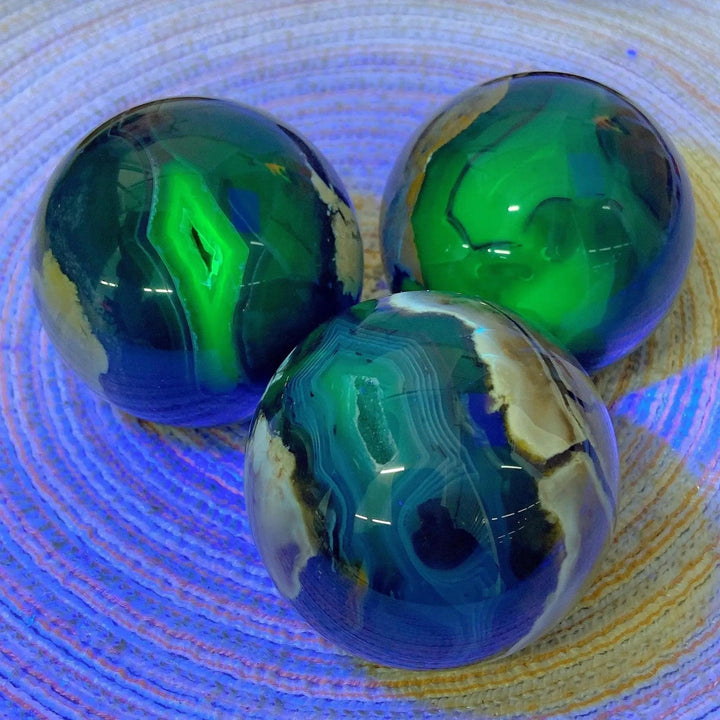Three polished Volcanic Agate Spheres, UV reactive, showcasing vibrant green, blue, and earthy bands, grounding and transformative.