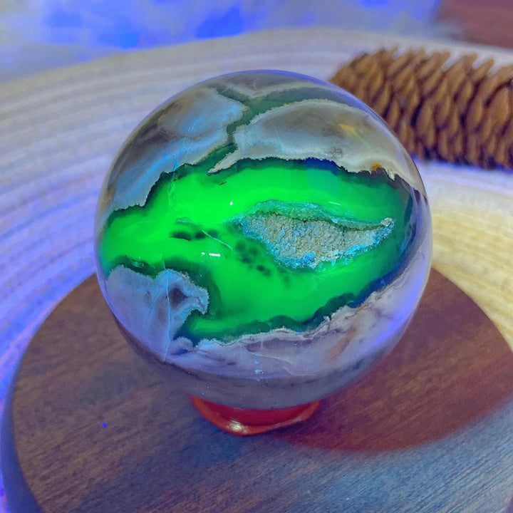 Volcanic Agate Sphere, a UV reactive crystal ball with vibrant green fluorescence and earthy banding, on a wooden stand.