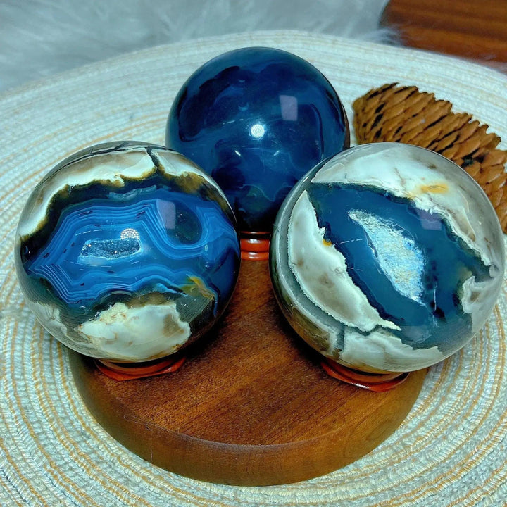 Three Volcanic Agate Spheres, one deep blue and two with striking blue, white, and brown banding, on a wooden stand.