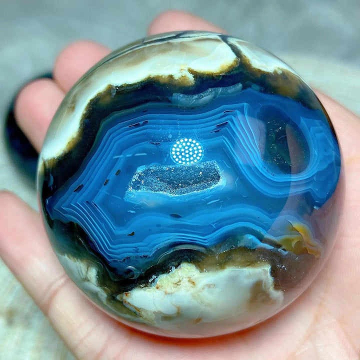 Volcanic Agate Sphere, a UV reactive crystal ball with concentric blue, white, and brown bands, held in a hand.