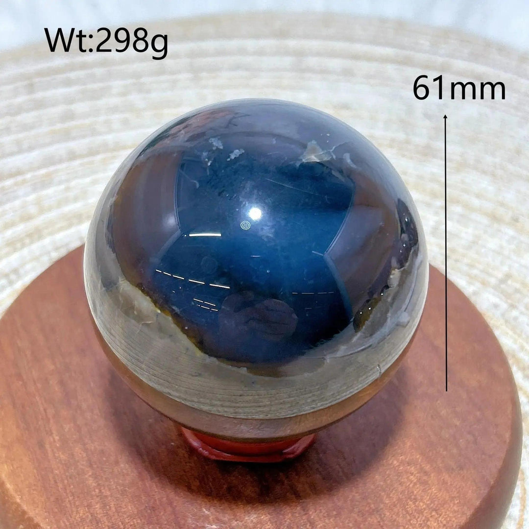 Volcanic Agate Sphere, a 61mm, 298g UV reactive crystal ball with deep blue and earthy bands, on a wooden stand.