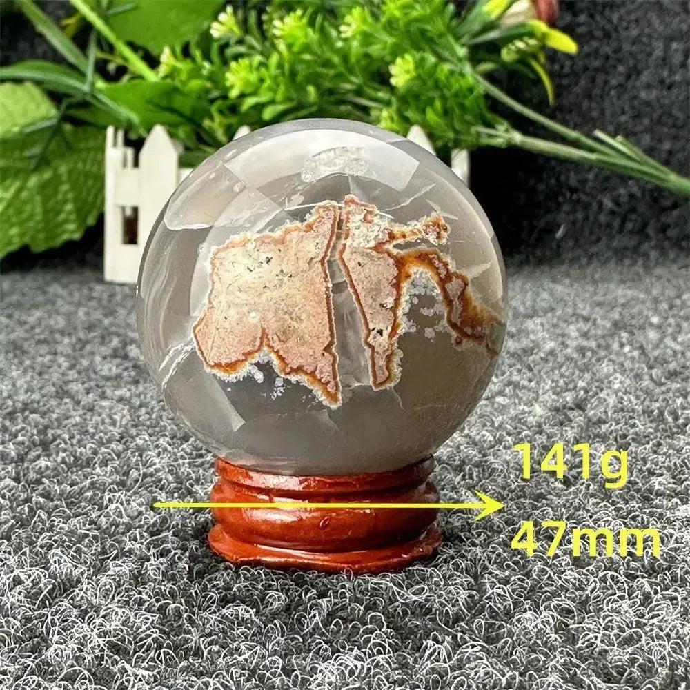 Volcano Agate sphere by Crystal Destiny, featuring fiery red-brown patterns within clear agate, on a wooden stand.