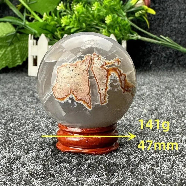 Volcano Agate sphere by Crystal Destiny, featuring fiery red-brown patterns within clear agate, on a wooden stand.