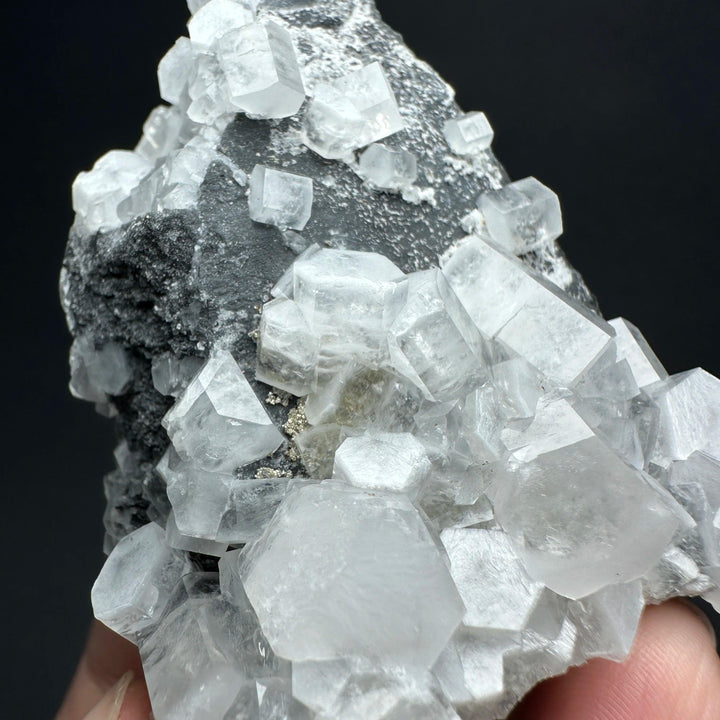 Raw white calcite crystal cluster specimen with cubic healing stones on dark matrix rock.