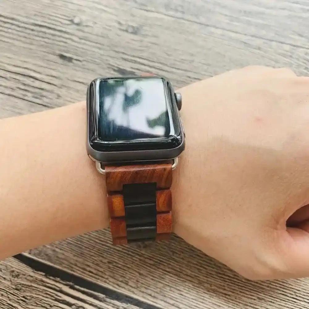 Handcrafted dark brown and black wooden Apple Watch band with silver hardware worn on a wrist.