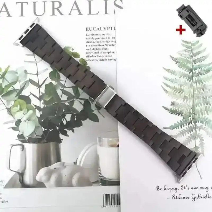 Dark brown wooden Apple Watch band with silver clasp, shown on a magazine with eucalyptus leaves.