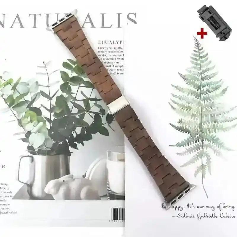 Handcrafted dark brown wooden Apple Watch band with silver-tone clasp, displayed on a nature-themed background.