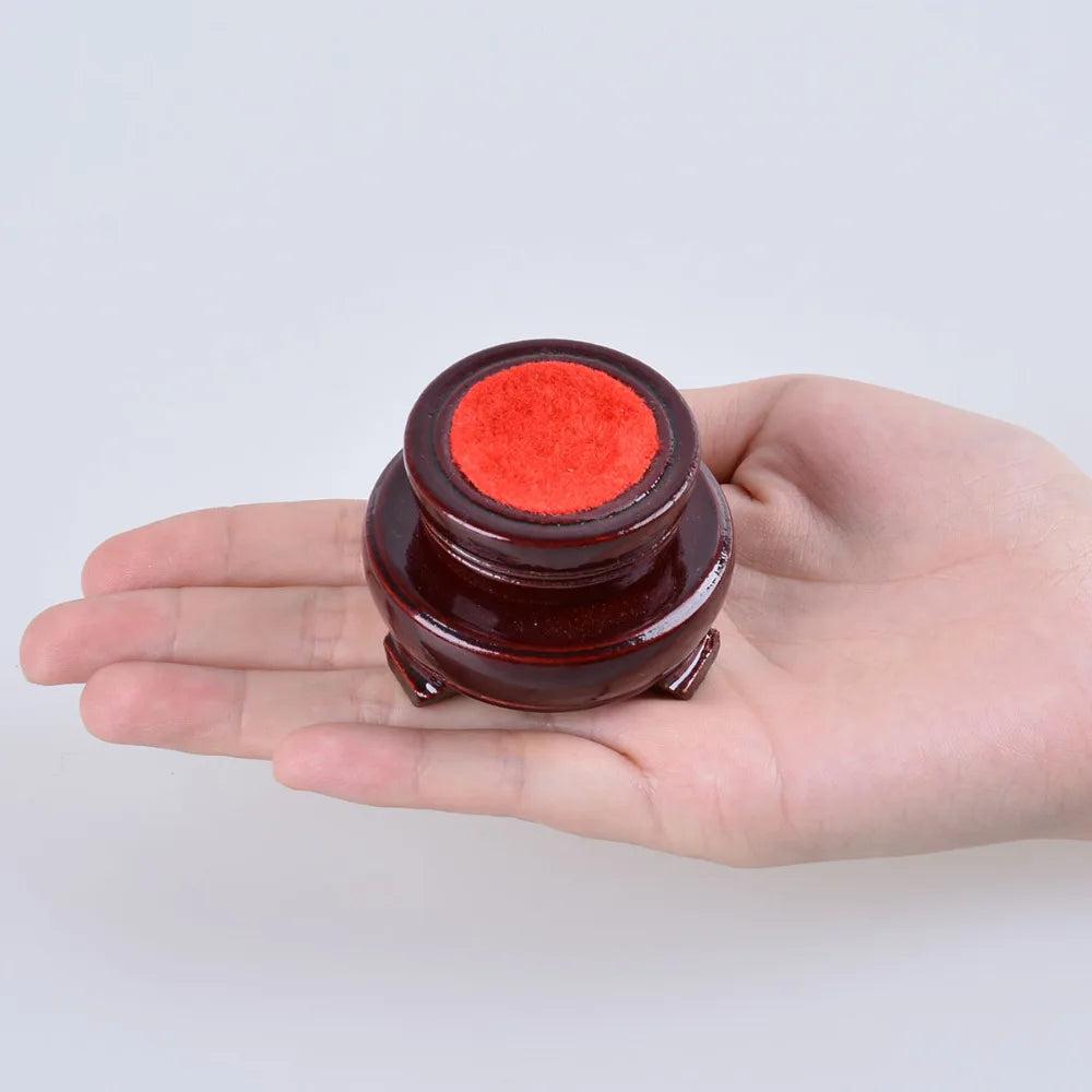 Small, dark brown wooden crystal ball display stand with a red felt top, held in an open palm.