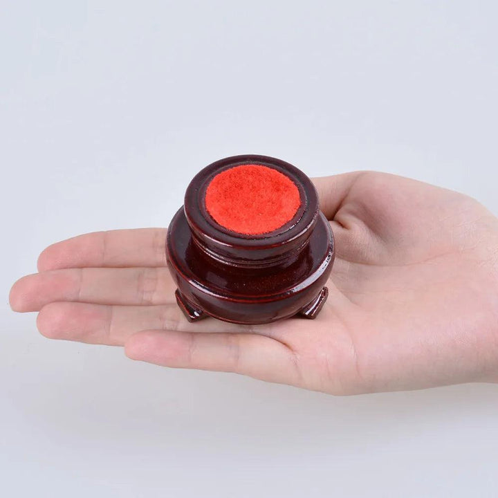 Small, dark brown wooden crystal ball display stand with a red felt top, held in an open palm.