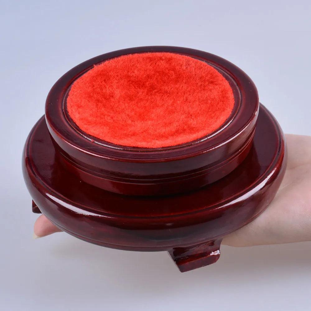 Dark red wooden crystal ball display stand with a plush red velvet top, held in a hand.
