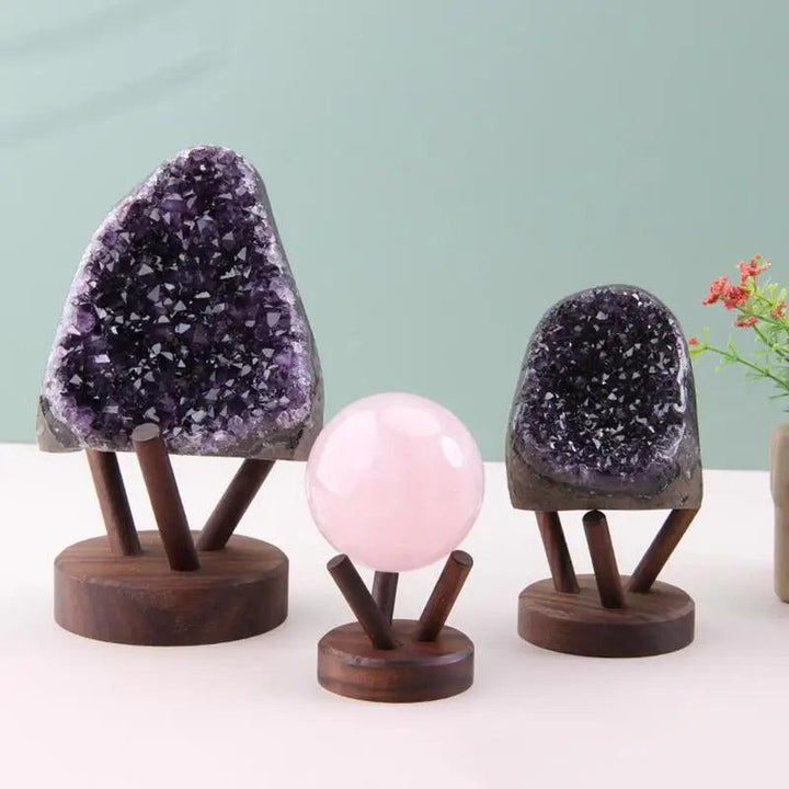 Dark wood display stands holding two purple amethyst geodes and a pink rose quartz sphere.