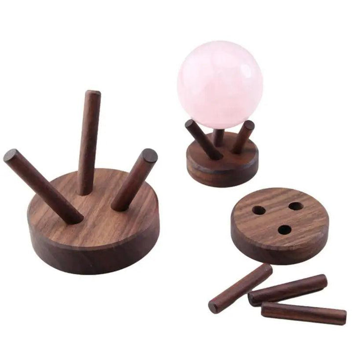 Dark wood crystal display stand rack holding a pink rose quartz sphere, with a disassembled stand nearby.