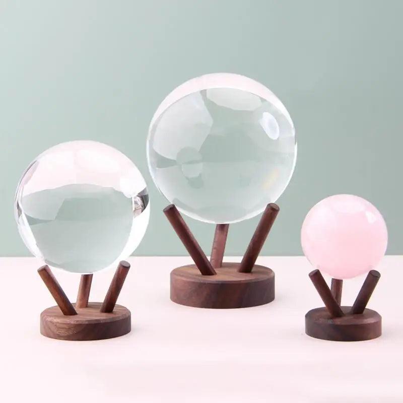 Three wooden display stands holding clear and pink crystal spheres, in small, medium, and large sizes.