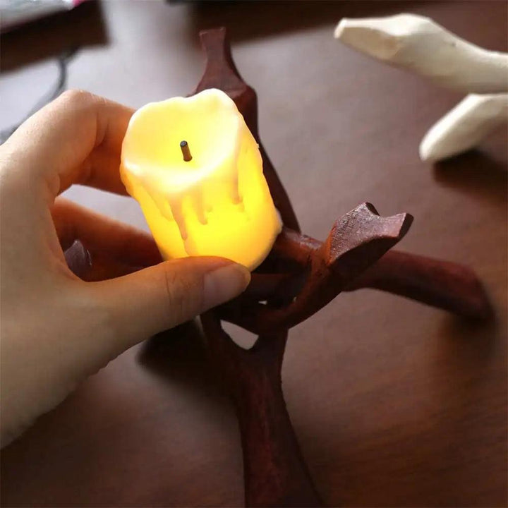 Hand placing a glowing LED candle on a dark brown natural wood tripod display stand.