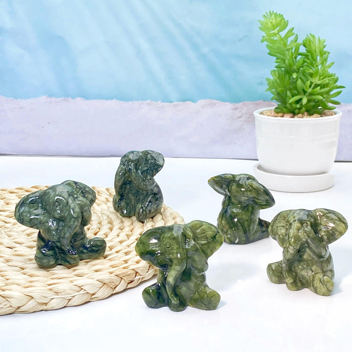 Five small, deep green Xiuyan Jade elephant carvings on a woven mat, symbolizing luck, wisdom, and protection.