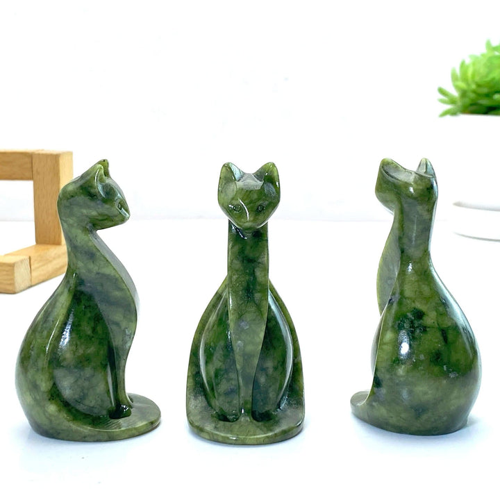 Three polished Xiuyan jade Egyptian cat carvings, dark green with natural patterns, for home decor.