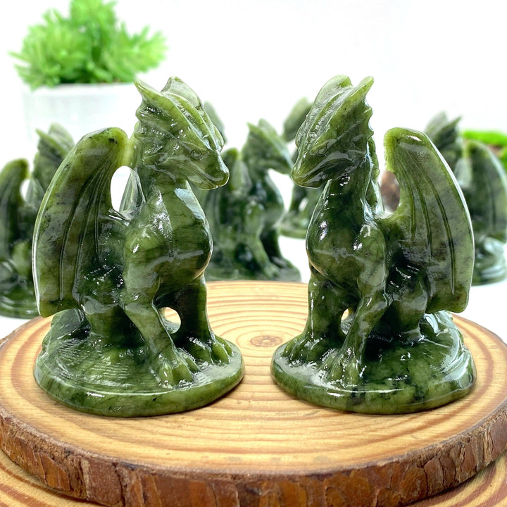 Two vibrant green Xiuyan Jade dragon carvings, detailed with wings, sitting on wooden bases.
