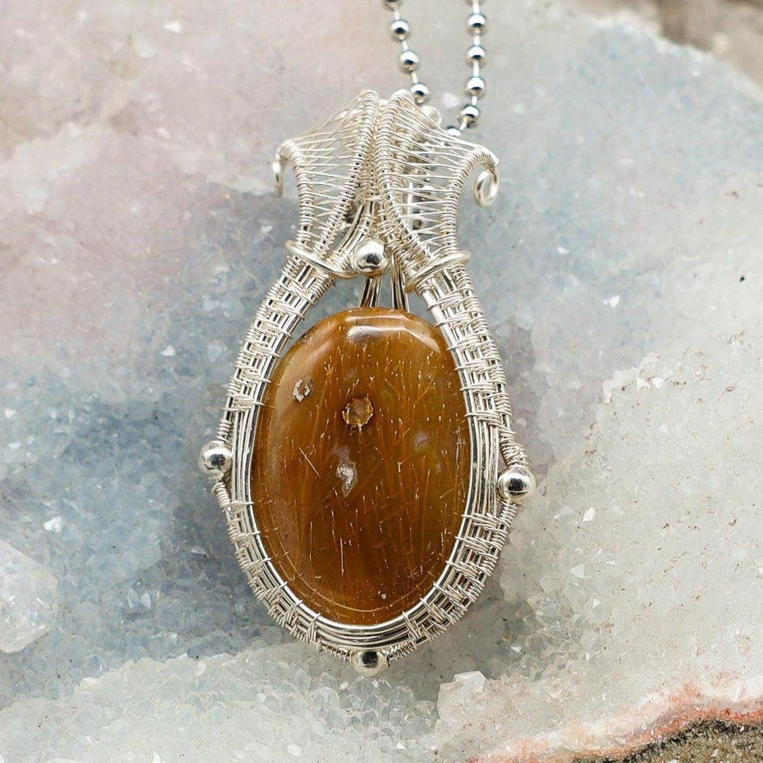 Handcrafted copper wire wrap pendant with a brown oval crystal, promoting forgiveness and inner peace.
