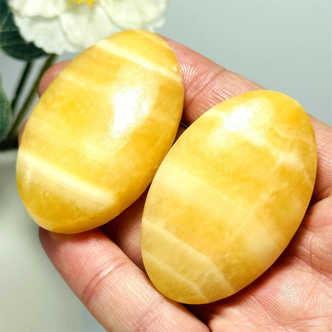 Two polished yellow calcite crystal palm stones with natural bands, held in a hand for meditation.