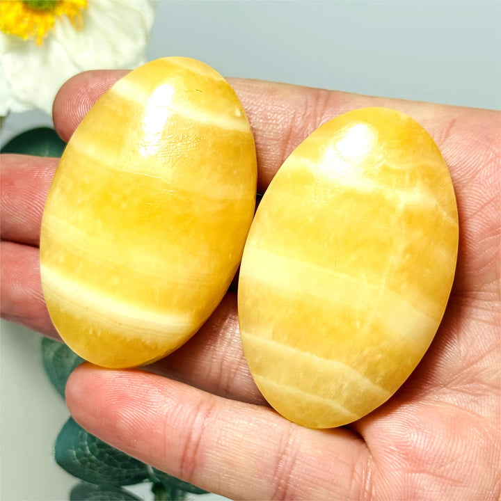 Two polished, oval yellow calcite palm stones with natural banding held in a hand for meditation.
