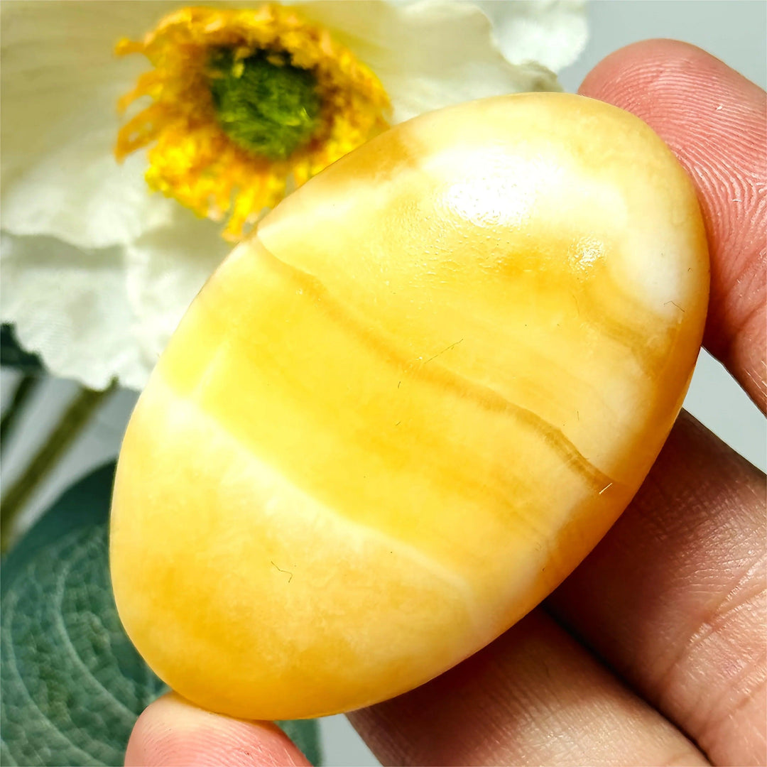Smooth yellow calcite crystal palm stone held in hand, perfect for healing and home decor.