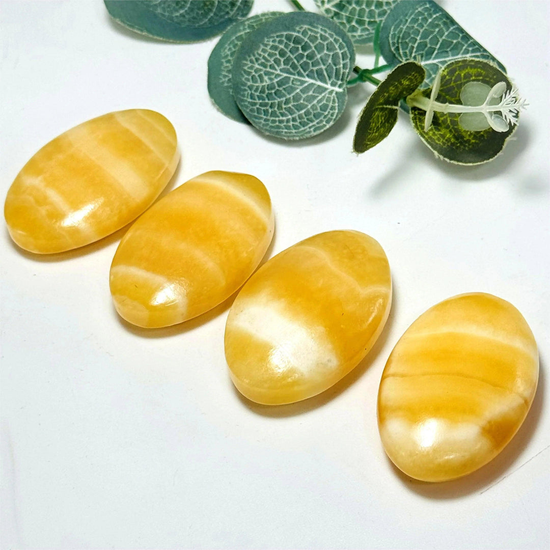 Four polished, oval yellow calcite palm stones with natural white banding, ideal for healing and decor.