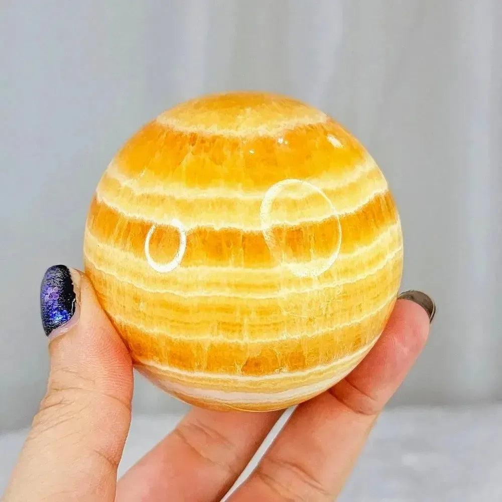Polished Yellow Calcite Honey Calcite Sphere with warm honey-golden tones and natural banding, held in hand.