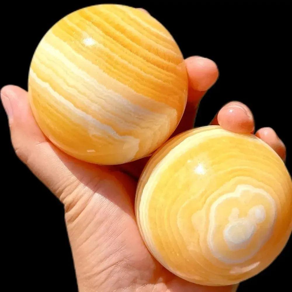 Two polished Yellow Calcite Honey Calcite spheres with warm golden banding, held in a hand. Crystal Destiny.