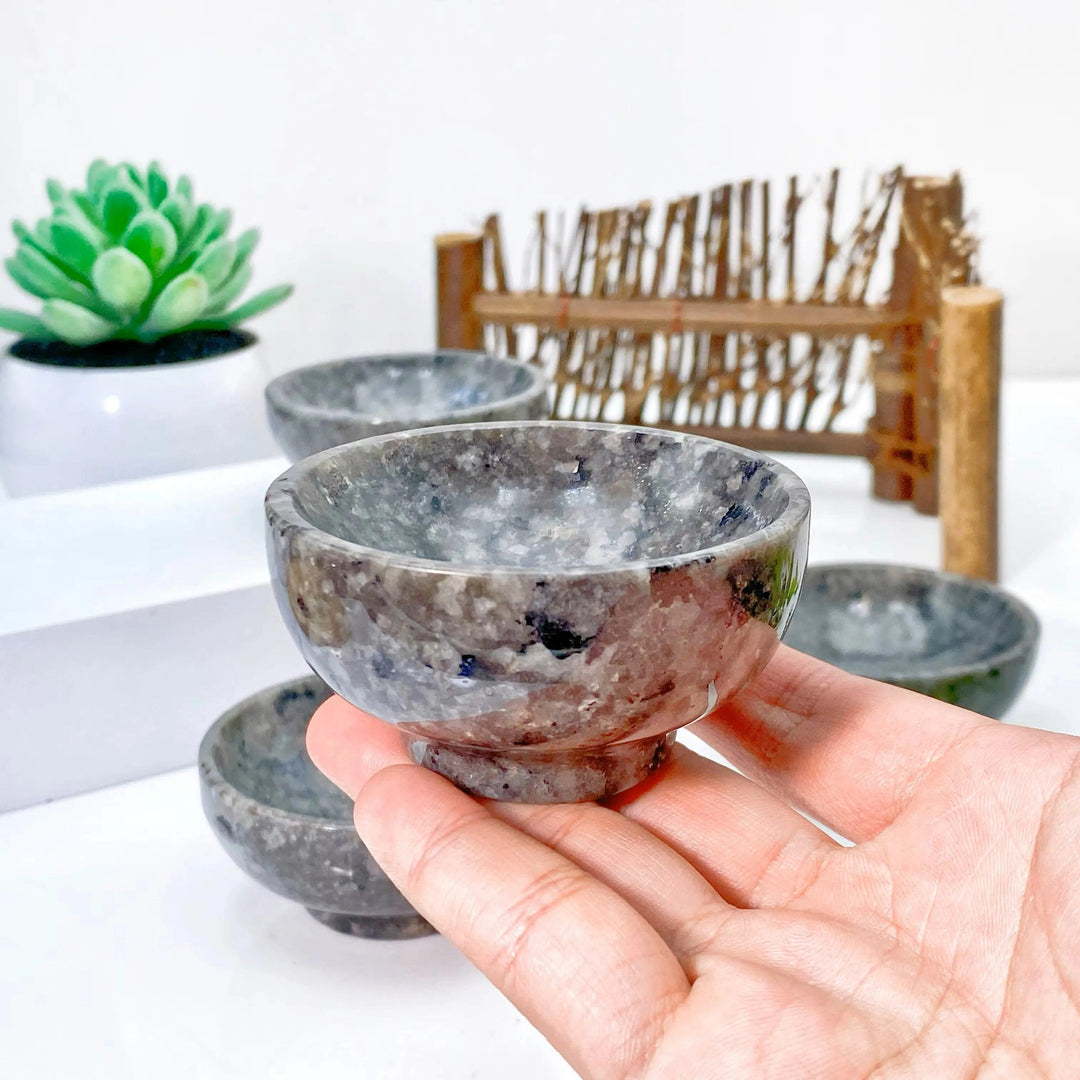 Hand holding a small, polished grey Yooperlite crystal bowl, showcasing its unique speckled texture and grounding presence.